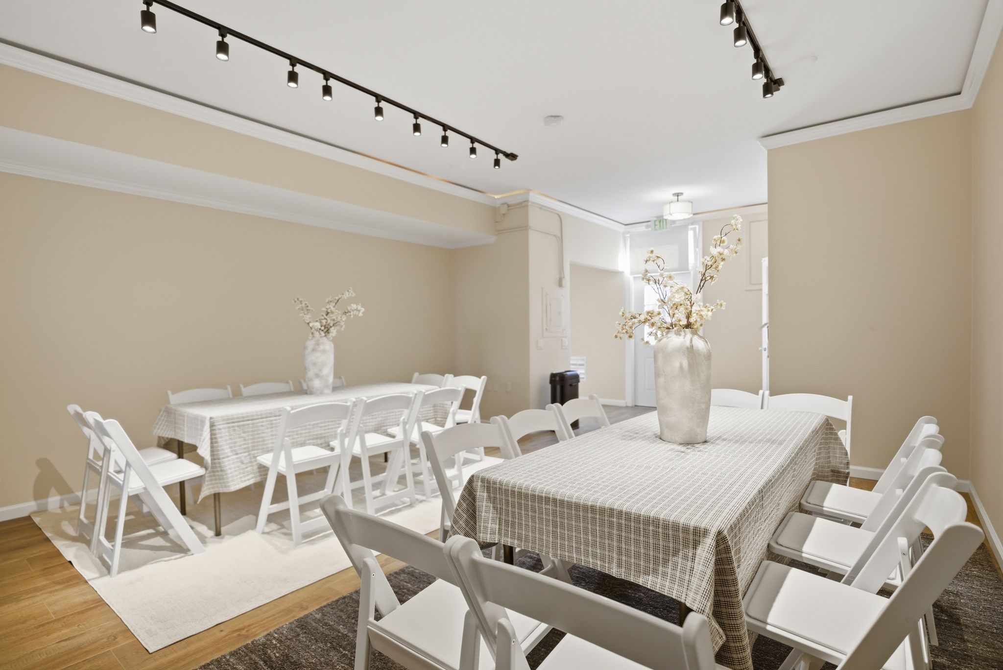 Event room set with two long tables, white chairs, and track lighting